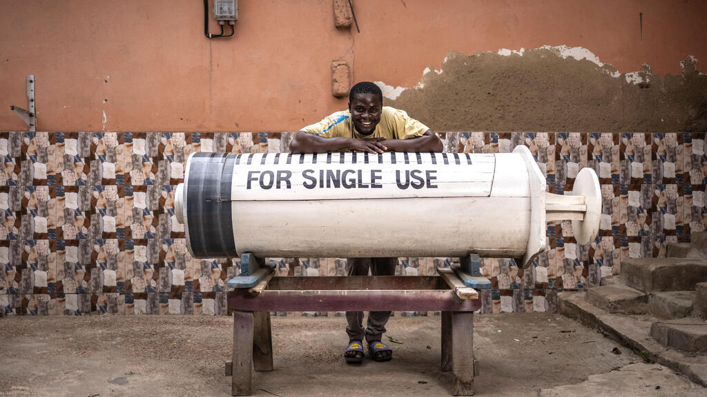 Coffin maker Lawrence Anang, 26, beside a syringe-shaped coffin commissioned for a doctor (Photo: Olympia de Maismont/AFP) גאנה ארונות קבורה מיוחדים יצרן ארונות הקבורה לורנס אנאנג בן 26 לצד ארון בצורת מזרק שעוצב כמחווה למקצועו של הנפטר רופא