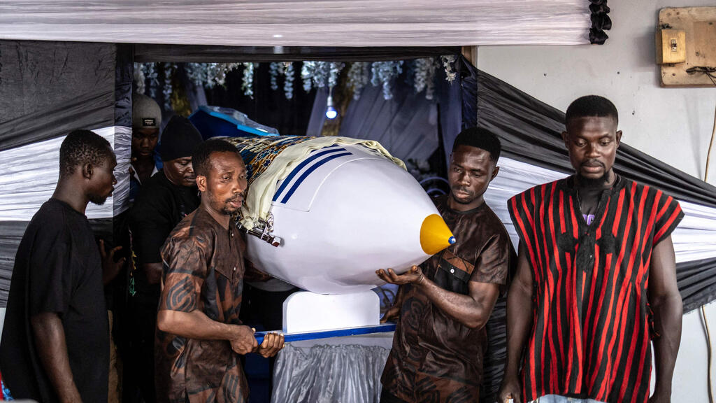Relatives gather beside the pen-shaped coffin built for Samuel Komi Tetteh (Photo: Olympia de Maismont/AFP) גאנה ארונות קבורה מיוחדים ארון קבורה בצורת עט המוכתם בדם כבשים של המורה הגנאי המנוח סמואל קומי טטה ב הלווייתו ב הלווייתו