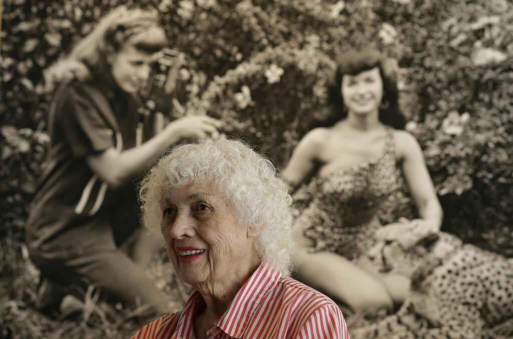 Bunny Yeager beside an image of herself photographing Bettie Page, 2013 (Photo: AP Photo/Lynne Sladky) באני ייגר לצד תמונה שלה מצלמת את בטי פייג', 2013