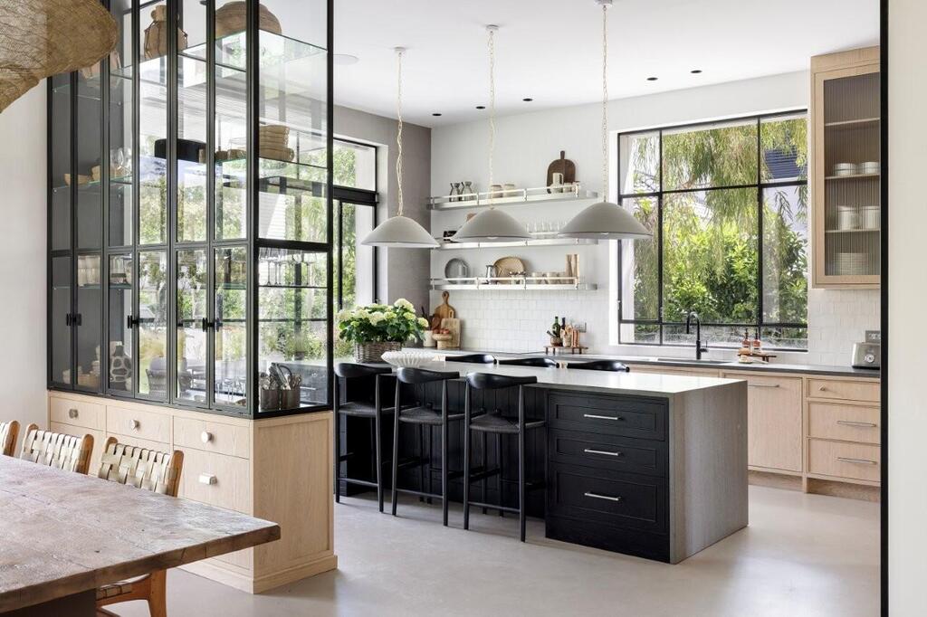 The kitchen pairs natural oak cabinetry with black accents, stainless-steel shelving and an oversized island (Photo: Itay Benit) The kitchen pairs natural oak cabinetry with black accents, stainless-steel shelving and an oversized island