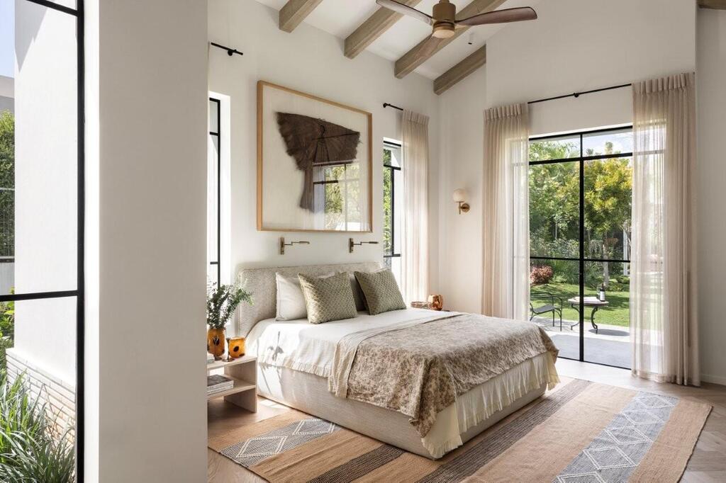 The primary bedroom features a pitched ceiling, exposed beams and floor-to-ceiling views of the garden (Photo: Itay Benit) The primary bedroom features a pitched ceiling, exposed beams and floor-to-ceiling views of the garden