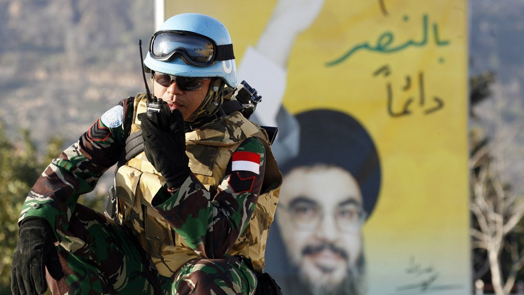 A UNIFIL member stands in front of a poster of Hezbollah leader Hassan Nasrallah in southern Lebanon 