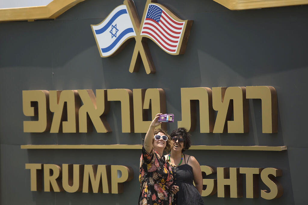 Two women taking a photo against sign at entrance to Trump Heights (Photo: Gettyimages) אנשים מצטלמים ליד שלט יישוב רמת טראמפ