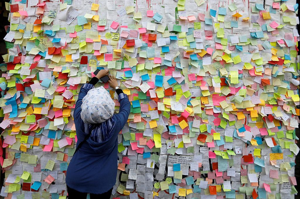 An Iraqi demonstrator pastes a note on the Wall of Wishes (Photo: Reuters ) קיר ה משאלות פתקים עיראק בגדד