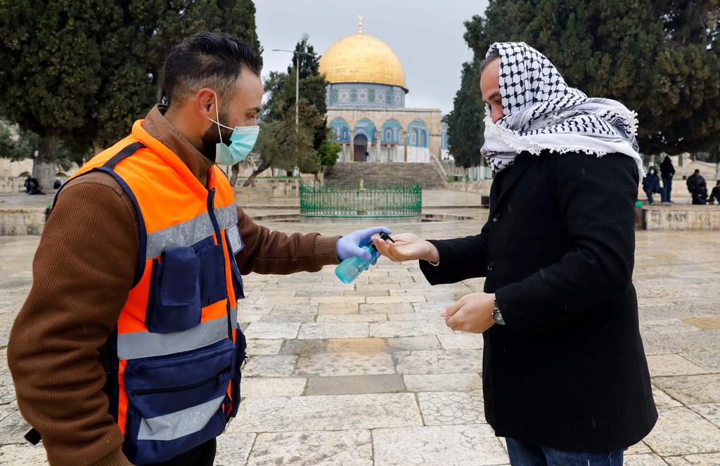 A volunteer sprays hand sanitizer for a Palestinian man on his way   to perform Friday prayers in the nearly deserted Al-Aqsa mosque   compound in the Old City of Jerusalem, March 20 2020 