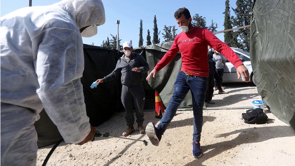 A Palestinian worker who returned from Israel being disinfected by a medical worker (Photo: EPA) חיטוי של עובד שעבר במעבר תרקומיא
