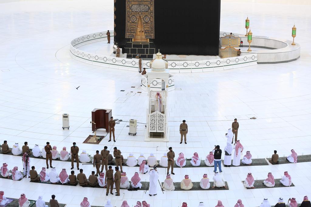 An Imam in a podium while Saudi security forces members, some clad in masks due to the COVID-19 coronavirus pandemic, stand between rows of worshippers gathering before the Kaaba at the Grand Mosque in Saudi Arabia's holy city of Mecca to attend the prayers of Eid al-Fitr 