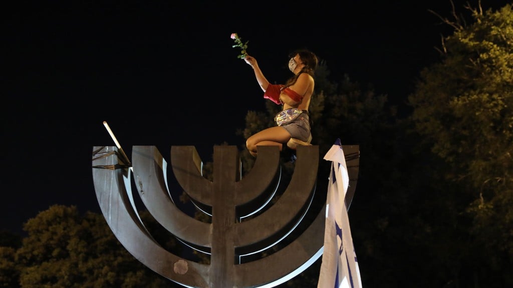 המפגינה חשופת החזה על פסל המנורה (צילום: EPA) ההפגנה מול הכנסת