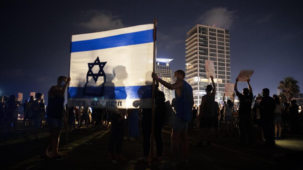 Protesters hold the Israeli national flag during a protest against Israel's Prime Minister Benjamin Netanyahu in Tel Aviv