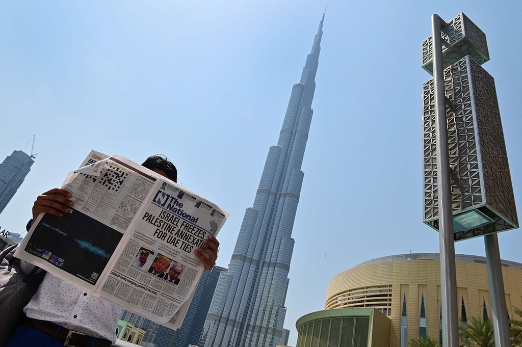 Man reading local newspaper announcing Israel-UAE ties with Dubai's Burj Khalifa in the background 