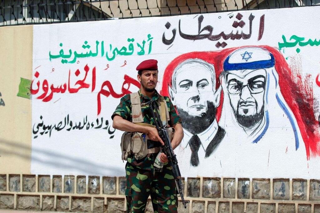 A Houthi fighter stands next to a mural in Yemen's capital Sanaa denouncing the UAE and Israeli leaders for their new bilateral ties 