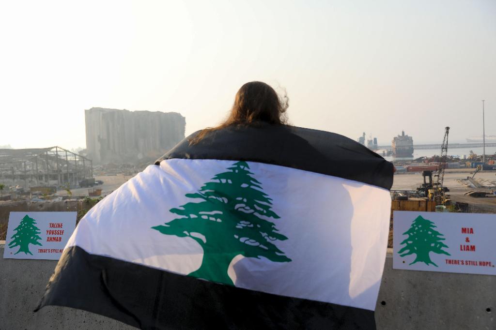 A woman, draped in a black-striped Lebanese flag, looks at the site of the massive explosion at Beirut's port area, during a demonstration to mark one month since the cataclysmic August 4 explosion 