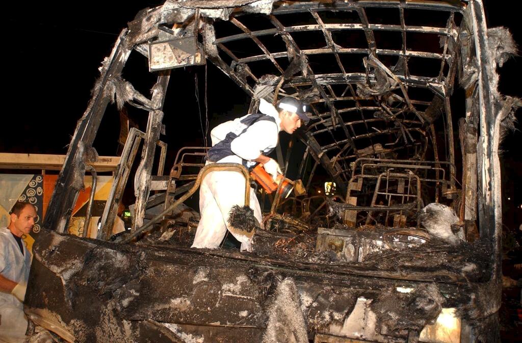 Rescuer examines the charred remains of a bus blown in a suicide bombing during the Second Intifada (Photo: Elad Gershgorn) אוטובוס אגד שהתפוצץ בצומת כרכור