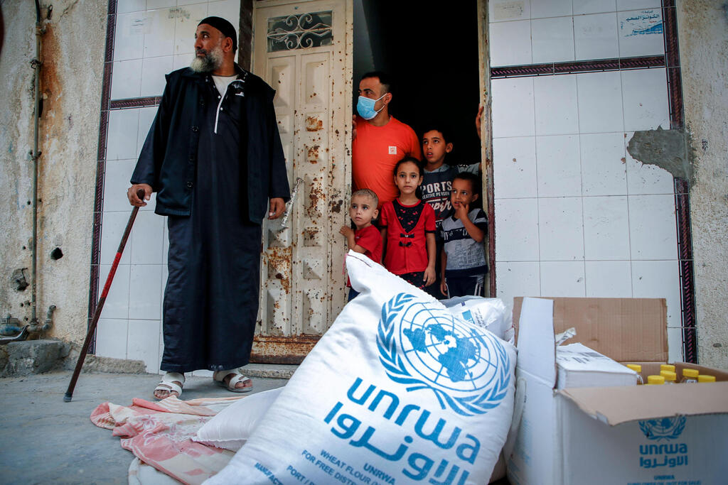 Members of a Palestinian family, some clad in mask due to the COVID-19 coronavirus pandemic, stand through the door of their home as they receive food aid provided by the United Nations Relief and Works Agency for Palestine Refugees (UNRWA) in Gaza