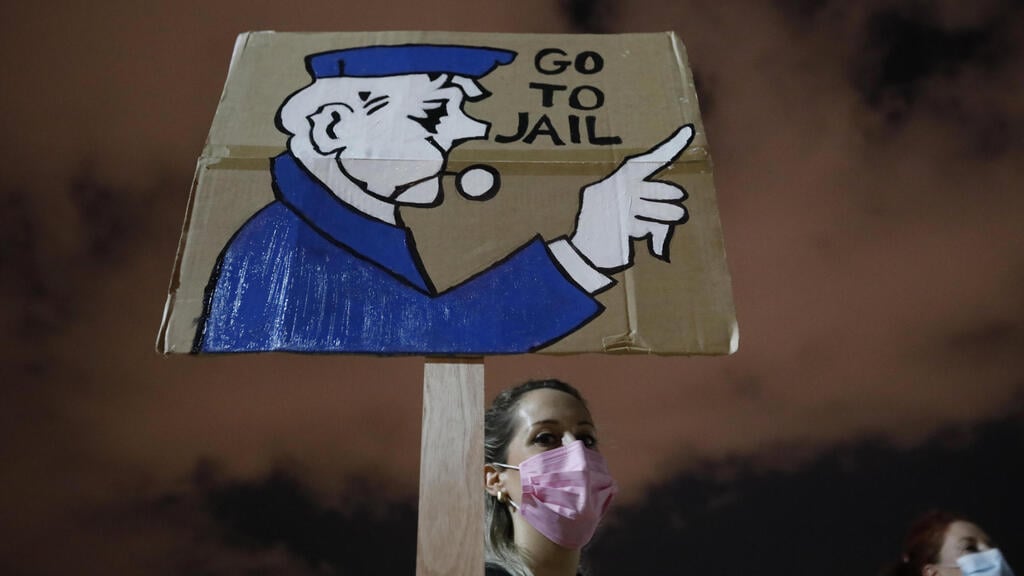 A demonstrator holds up a banner during a protest against Benjamin Netanyahu in Tel Aviv (Photo: AP) כיכר הבימה