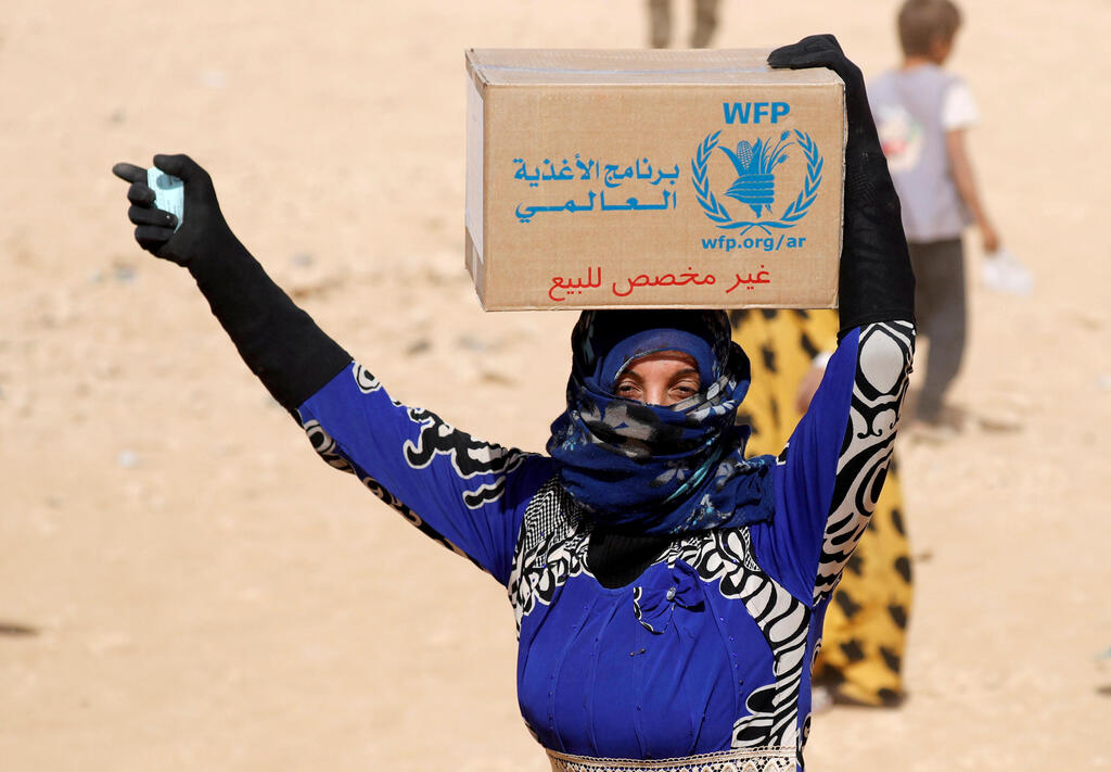 Woman displaced from fighting between the Syrian Democratic Forces and Islamic State militants holds a food stamp and carries a box of food aid given by the UN World Food Programme at a refugee camp in Ain Issa, Syria October 10, 2017