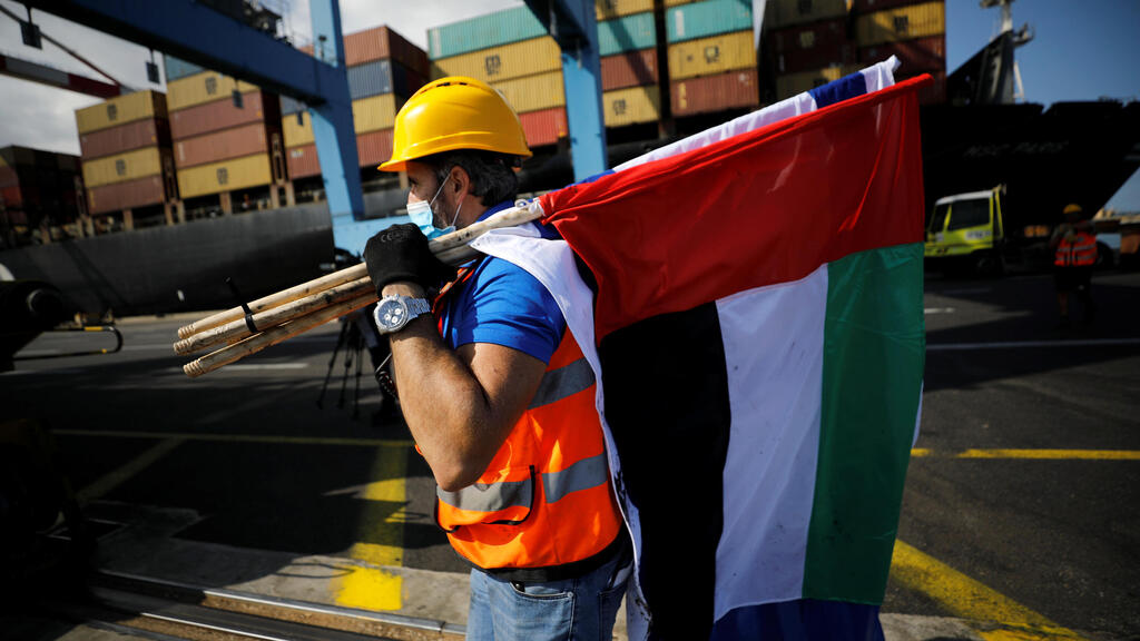 A worker carries Israeli and Emirati flags, after containers carrying goods from the United Arab Emirates, which entered Israel on an MSC cargo ship, were unloaded at Haifa's port