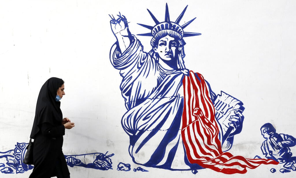 An Iranian woman walk past a mural depicting a defaced Statue of Liberty on the wall of former US embassy in Tehran, Iran
