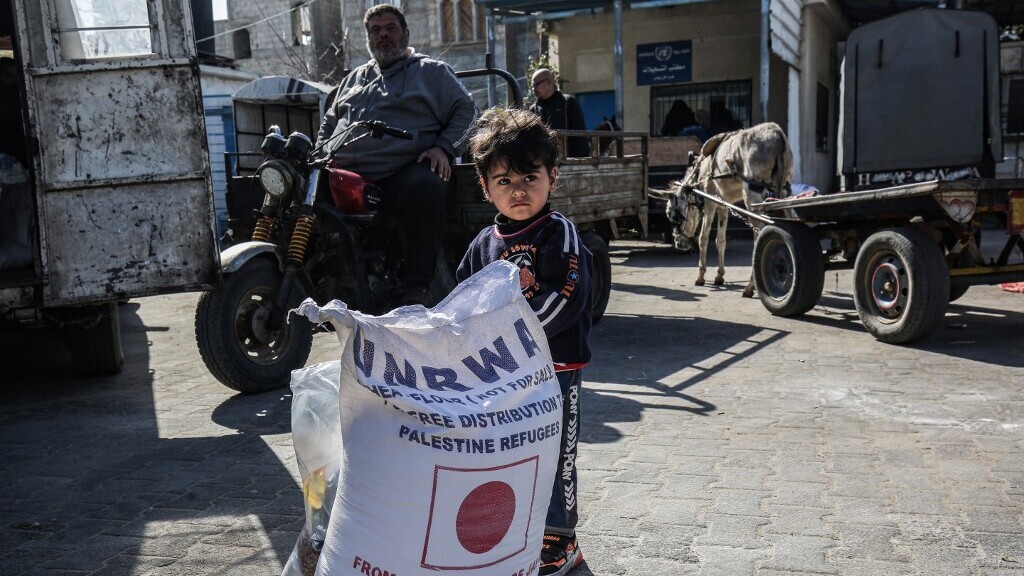 a child stands next to a sack of flour as people come to receive food aid from a United Nations Relief and Works Agency (UNRWA) distribution center in Khan Younis in the Gaza Strip 