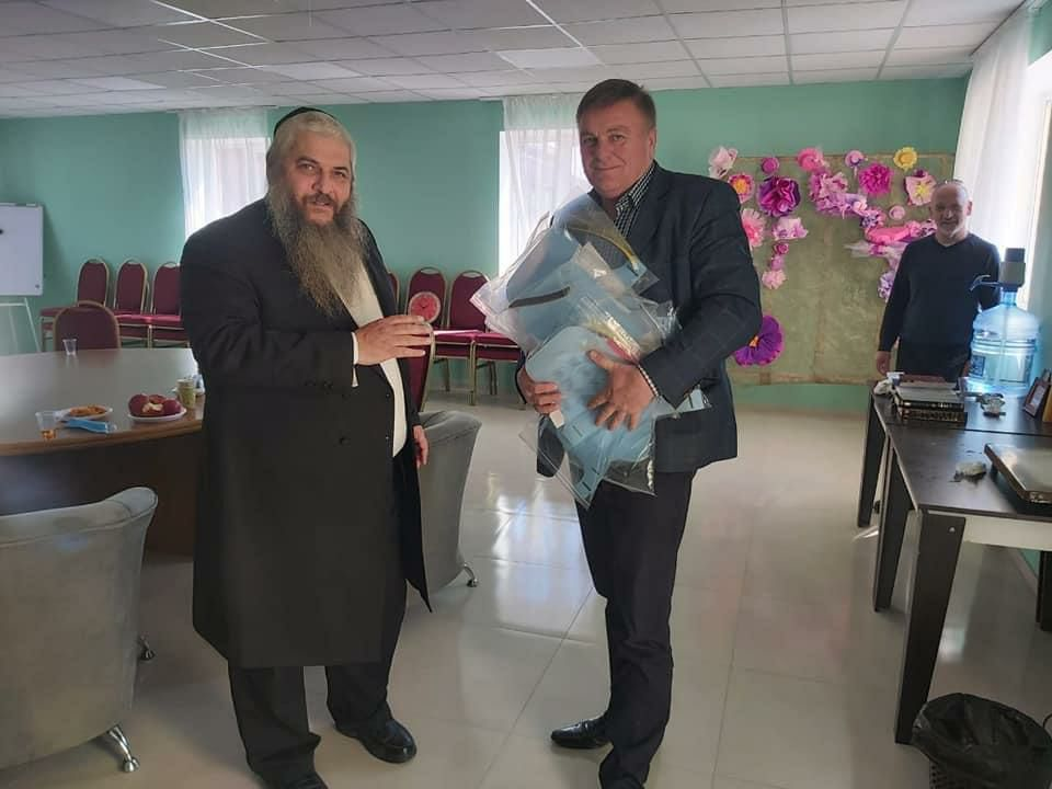 הרב משה ראובן אסמן מוסר לנציג בית החולים את חליפות המגן שייצרו יהודי אנטבקה (צילום: אדוארד דוקס, שמואל אסמן) הרב משה ראובן אוסמן חליפות מגן לנציג בית החולים
