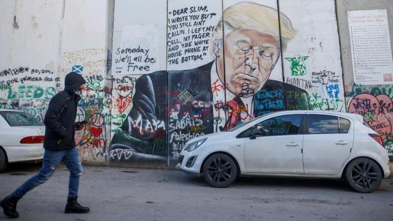 A Palestinian walks past a defaced mural painting of former US president Donald Trump on Israel's controversial separation barrier, which divides the West Bank from Jerusalem 