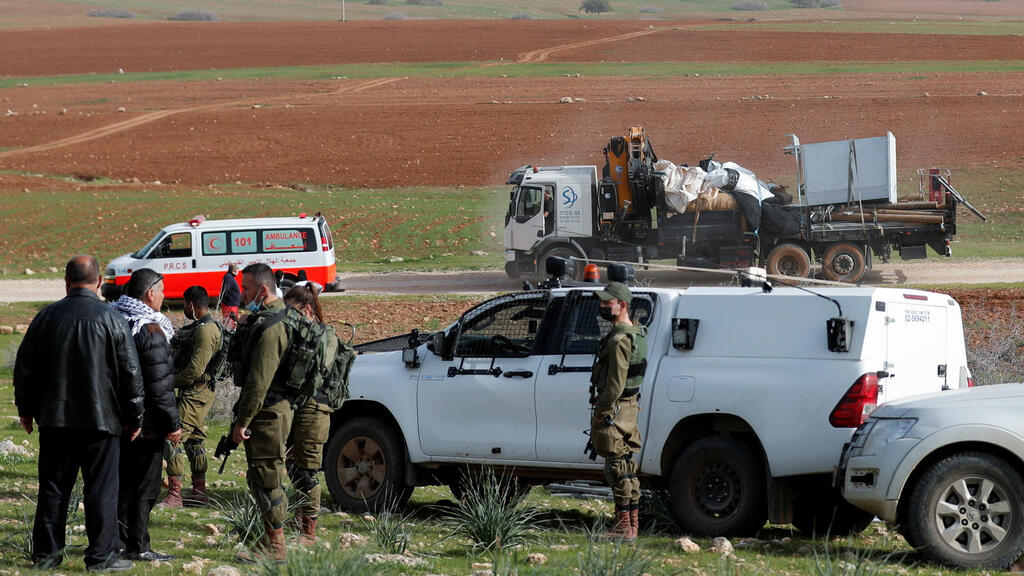 n Israeli truck carrying dismantled structures and tents belonging to Palestinians is seen as Israeli soldiers keep guard in the village of Khirbet Humsah