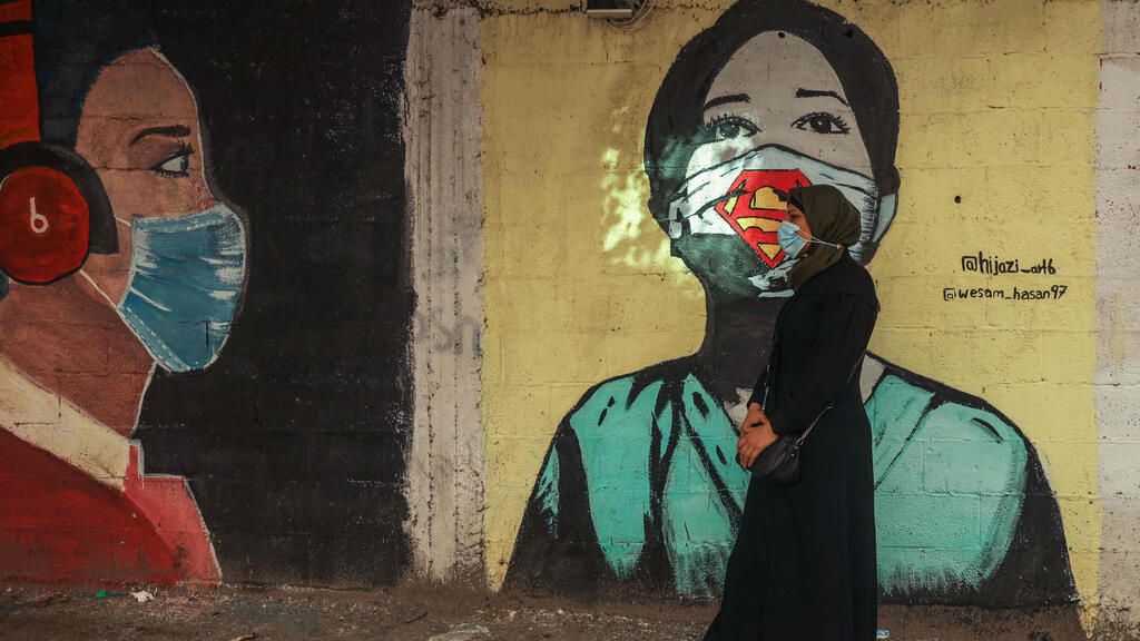 A Palestinian women walks past a coronavirus-inspired mural along a street in Gaza