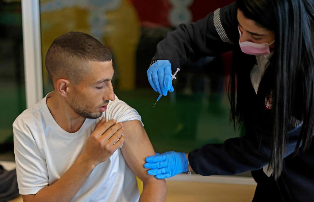 Health worker administers COVID-19 vaccine in Beit Shemesh (Photo: AFP) צעיר מתחסן חיסון חיסונים מתחסנים פייזר מגן דוד אדום מד"א בית שמש