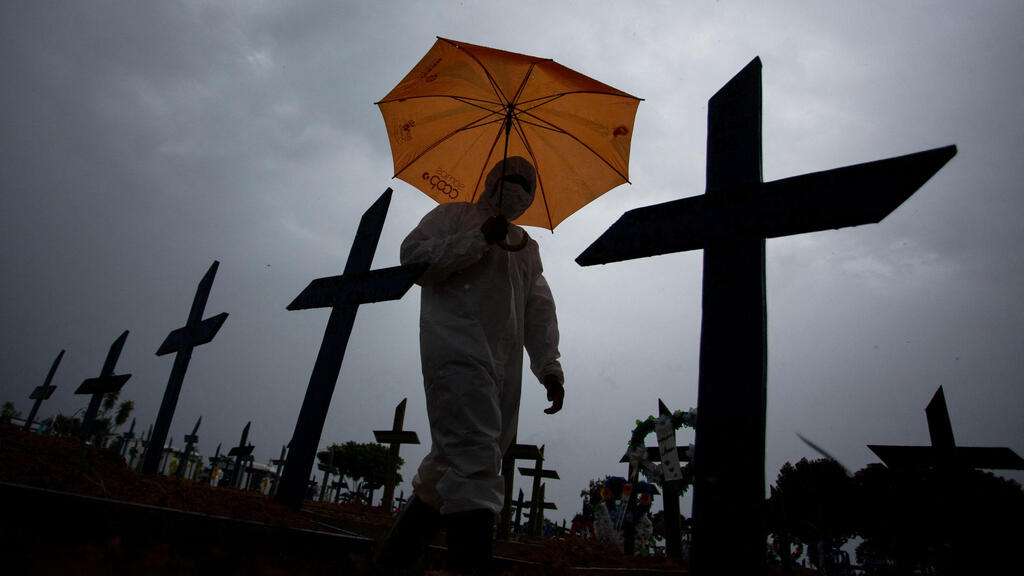  a worker wearing a protective suit and carrying an umbrella walks past the graves of COVID-19 victims at the Nossa Senhora Aparecida cemetery, in Manaus