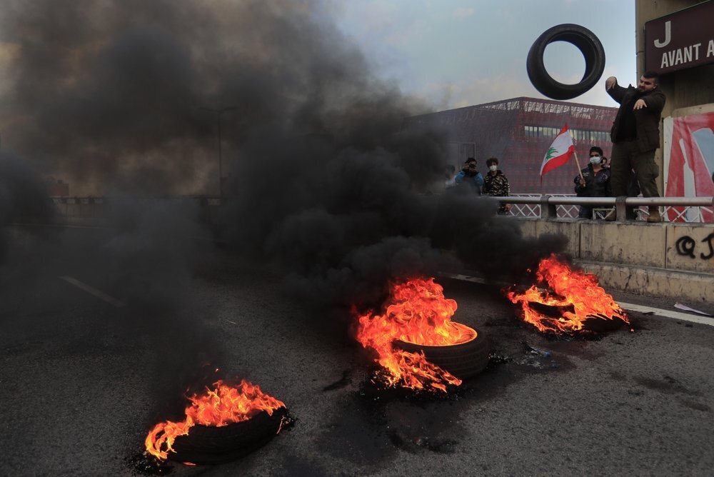 a protester throws a tire into burning tires to block a main highway, in the town of Jal el-Dib, north of Beirut, Lebanon 