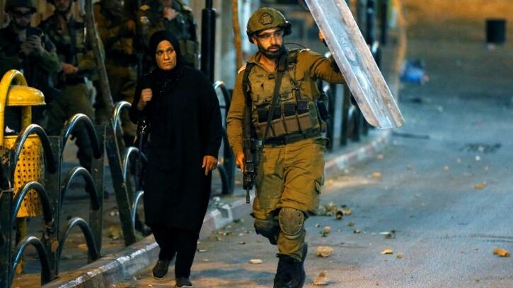 A Palestinian woman takes cover behind an Israeli soldier holding up his riot shield during clashes in the West Bank city of Hebron (Photo: AFP) A Palestinian woman takes cover behind an Israeli soldier holding up his riot shield during clashes in the West Bank city of Hebron