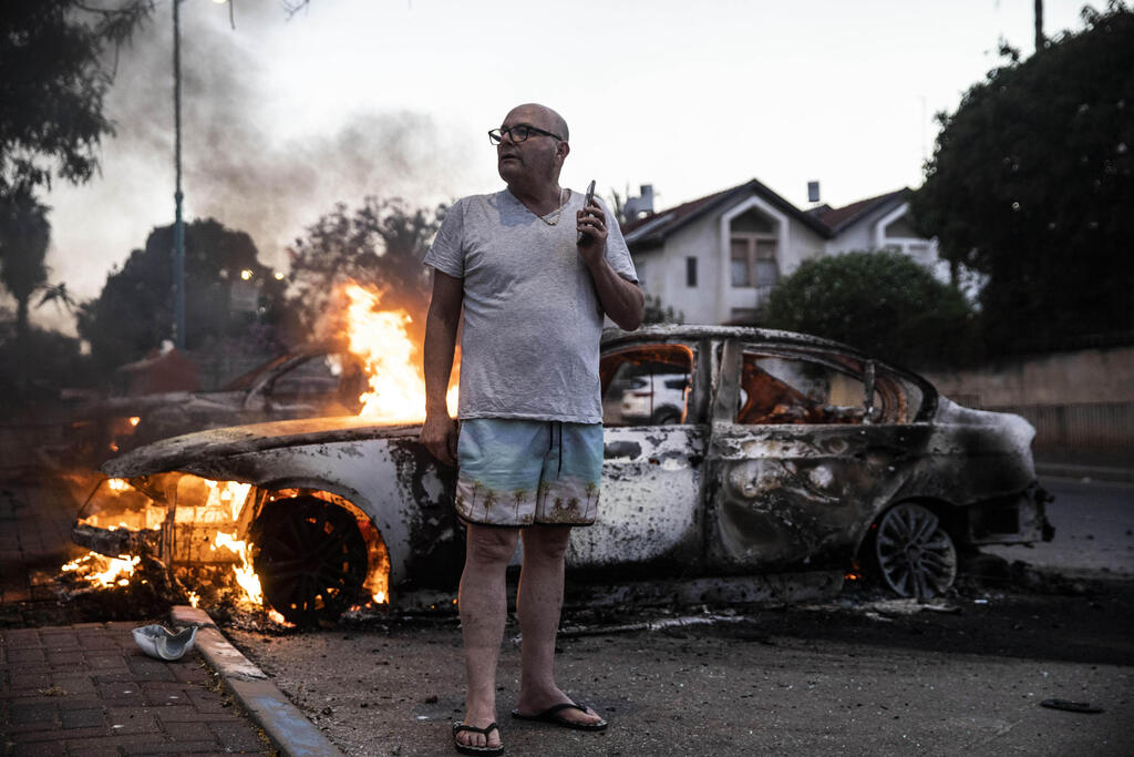 Man stands next to vehicle torched in Lod riots 