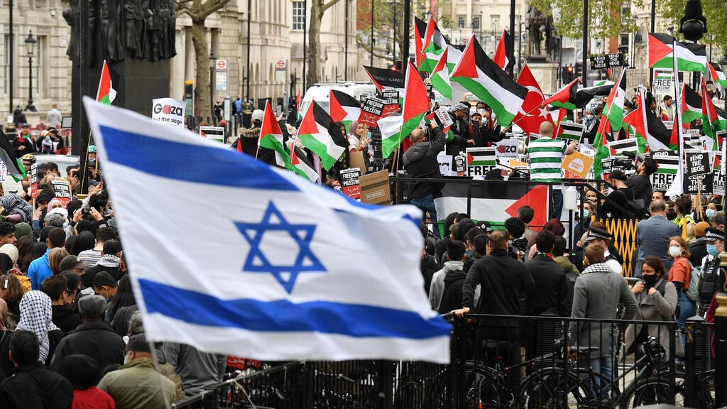An Israeli flag being waved in front of a crowd of pro-Palestinian protesters (Photo: AFP) מפגינים פרו-ישראלים מול הפגנת תמיכה ב פלסטינים לונדון בריטניה