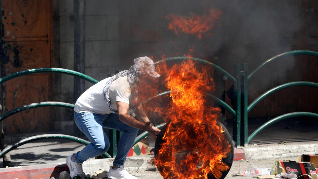 A Palestinian burns tires during clashes in Hebron last May (Photo: EPA) מהומות בחברון