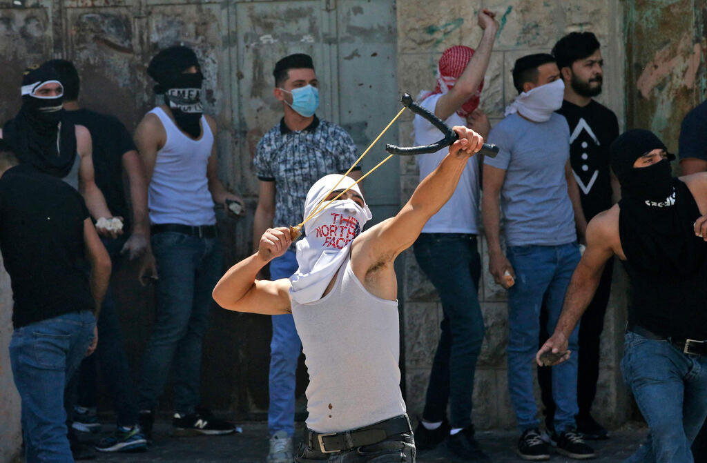 Palestinian rioter uses slingshot to hurl stones at troops in Hebron on Friday 