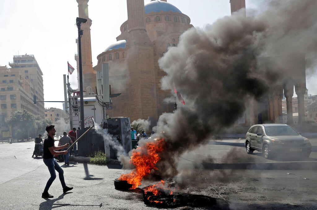 Lebanese forces watch anti-government protesters burn waste bins to block a highway that leads to the airport during a protest in Beirut (Photo: AFP) Lebanese forces watch anti-government protesters burn waste bins to block a highway that leads to the airport during a protest in Beirut, Lebanon, 26 June 2021