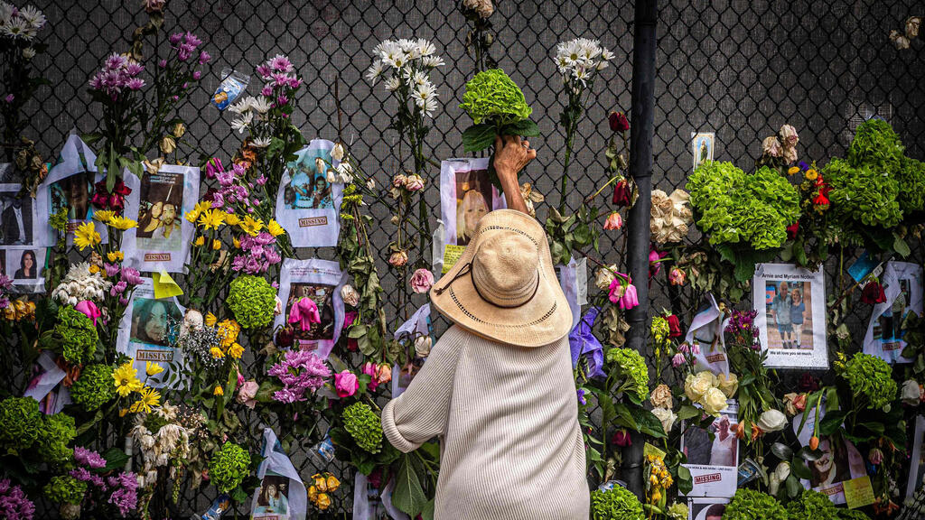 Woman places flowers on memorial near site of collapsed building in Surfside (Photo: AFP) פרחים ואירוע לזכר נספים ב אסון קריסה ב סרפסייד ליד מיאמי פלורידה ארה"ב