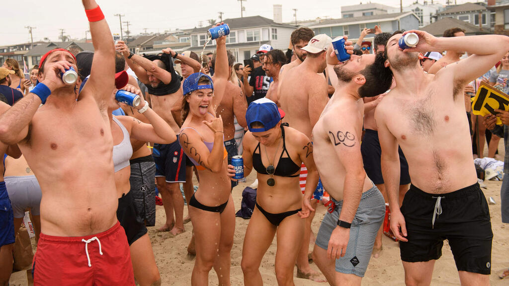 Participants chug beer on the beach during the 47th annual Hermosa Beach Ironman competition where participants must run a mile, paddle a surfboard a mile, and chug a six-pack of beer on July 4, 2021 in Hermosa Beach, California 