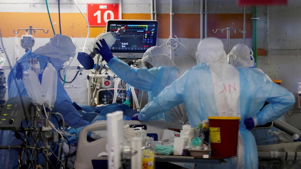 Medical workers attending to a COVD patient in Rambam Hospital's COVID ward (Photo: Reuters) Medical workers, seen through a window of an observation room, wear personal protective equipment (PPE) as they work inside an underground ward
