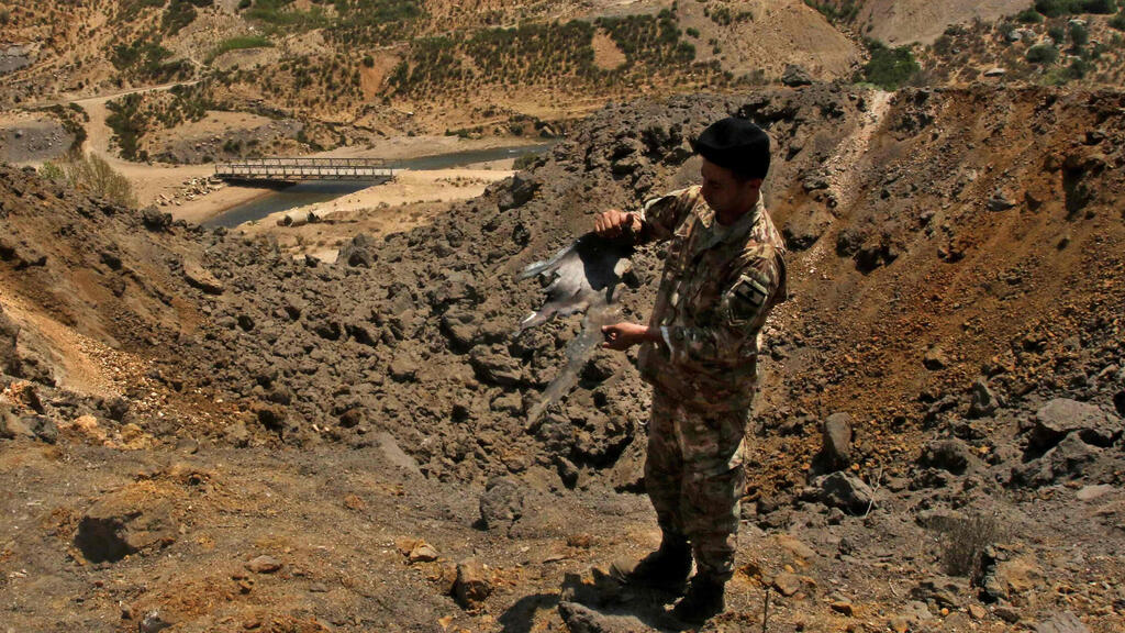 A Lebanese soldier holds up a purported fragment of an Israeli bomb as he stands beside a crater said made by an overnight IAF strike in southern Lebanon, August 5, 2021 
