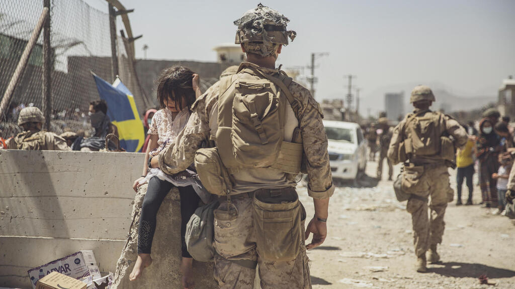 A marine cares for young child awaiting processing at an evacuation control checkpoint during an evacuation at Kabul airport 