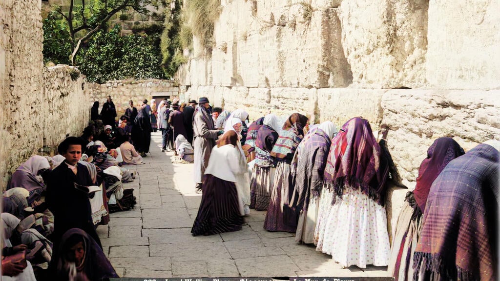Men and women praying together in front of the Western Wall in the early 1920s (Photo: The American Colony Photo Department, Color: MyHeritage) גברים ונשים מתפללים יחדיו מול הכותל המערבי בתחילת שנות ה-20. את הרחבה הגדולה המוכרת כיום חוסמים בתי שכונת המוגרבים, שנהרסו מיד בתום מלחמת ששת הימים