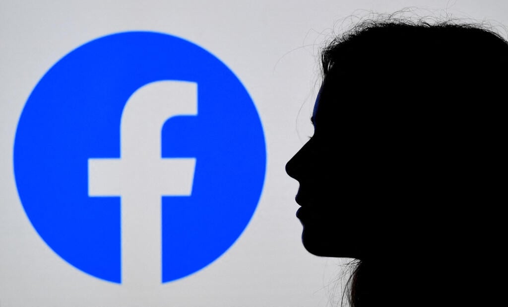 Facebook App logo displayed in the background (Photo: AFP) photo illustration, a person looks at a smart phone with a Facebook App logo displayed on the background