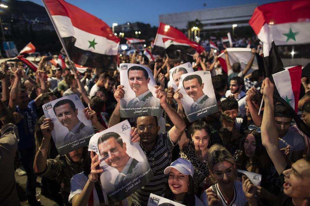 Syrian President Bashar Assad supporters hold up national flags and pictures of Assad as they celebrate at Omayyad Square, in Damascus, Syria 