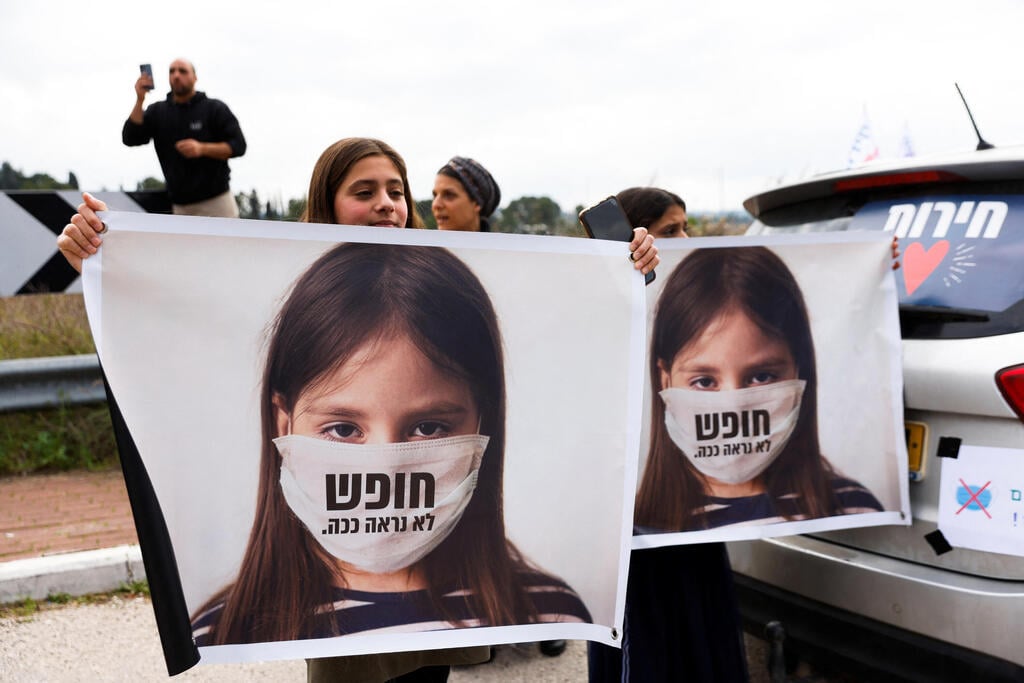 Anti-mandate protesters holding signs showing a picture of a girl in a mask, reading 'freedom doesn't look like this' in the 'Freedom Convoy', in Jerusalem, February 14, 2022 (Photo: Reuters) מפגינים נגד הגבלות הקורונה
