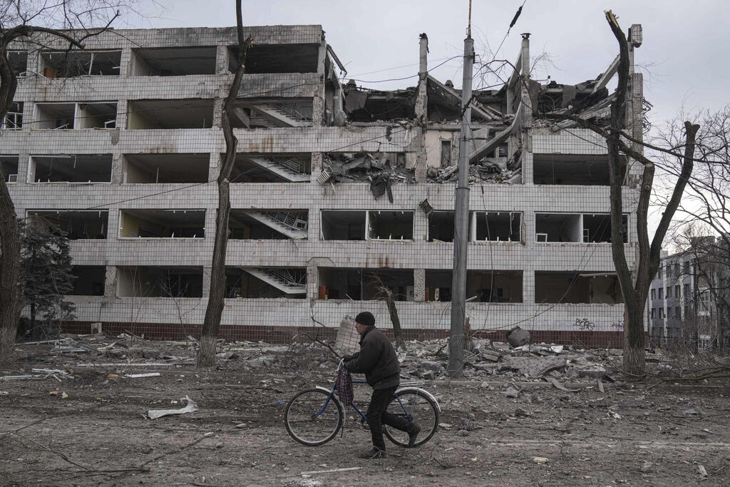 Man rides his bicycle next to a building heavily damaged in Russian shelling (Photo: AP) בניין הרוס במריופול