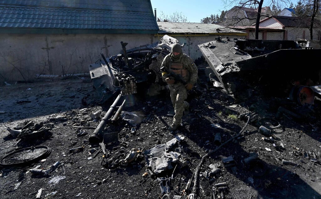 Soldier examines charred remains of armored vehicle, in Irpin, Ukraine (Photo: AFP) חיל בוחן שאריות נגמש משוריין באירפין משבר מלחמה רוסיה אוקראינה