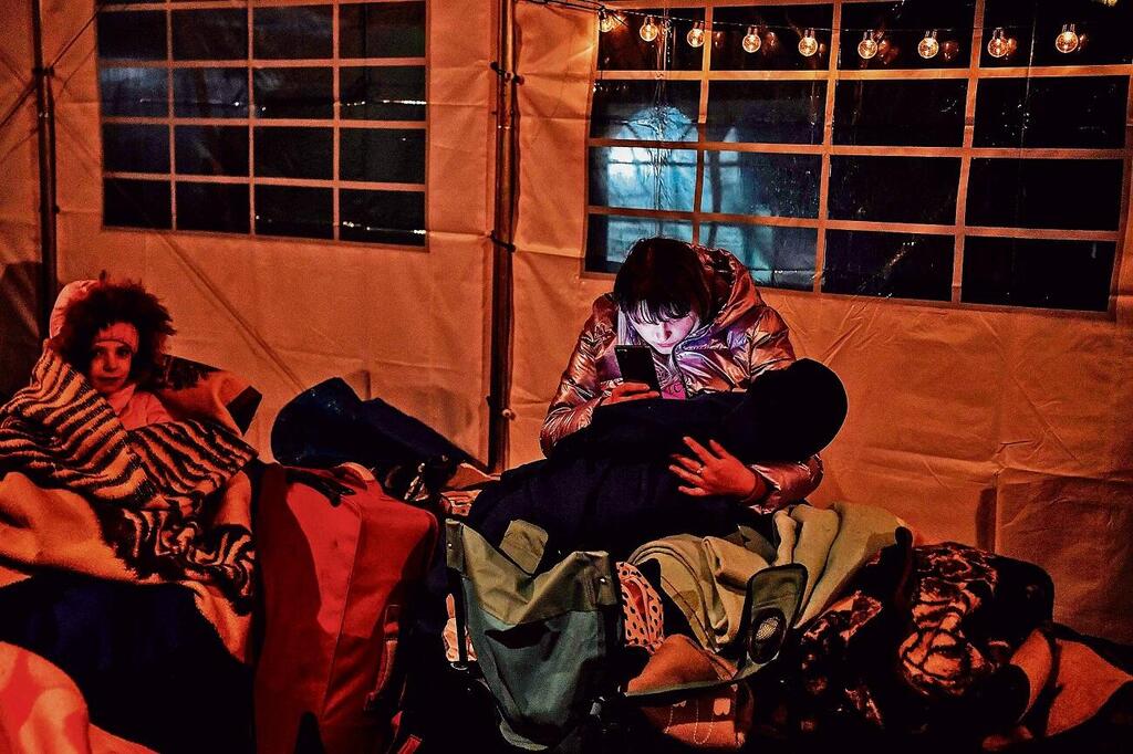 פליטה אוקראינית עם ילדה, מתעדכנת בחדשות בטלגרם במעבר הגבול עם פולין ( צילום: AFP) פליטה אוקראינית עם ילדה, מתעדכנת בחדשות במעבר הגבול עם פולין