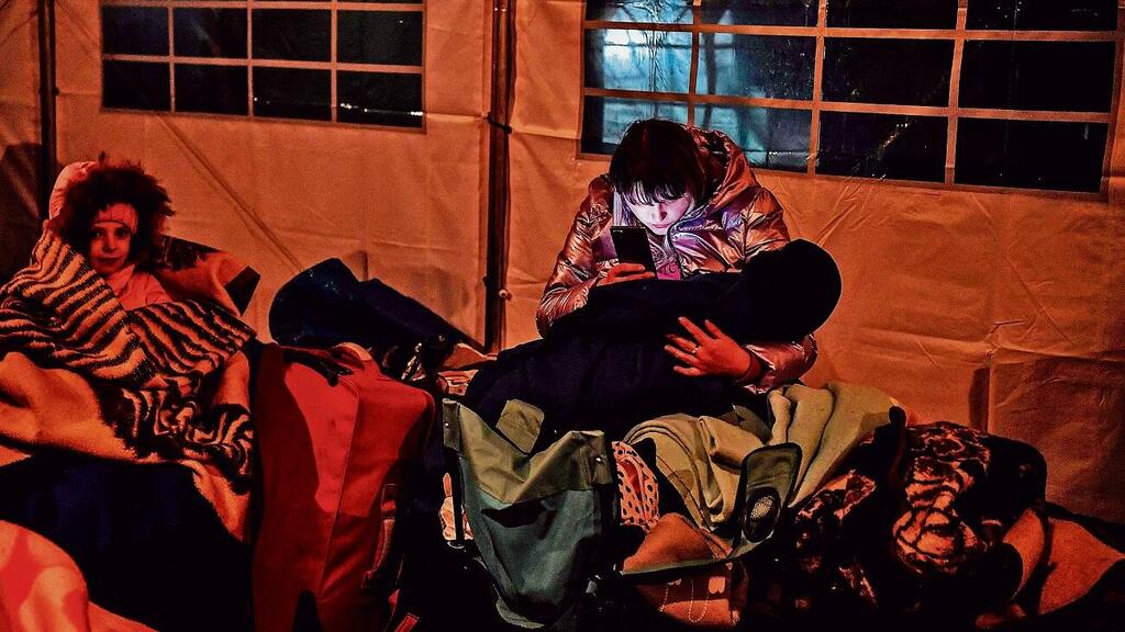 Ukranian refugee recieving updates via Telegram (Photo: AFP) פליטה אוקראינית עם ילדה, מתעדכנת בחדשות במעבר הגבול עם פולין