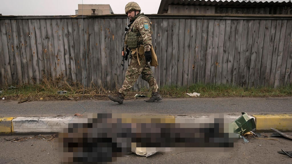 A Ukrainian soldier walks past a dead body on the streets of Bucha, Ukraine (Photo: AP) גופות ברחוב בבוצ'ה אוקראינה